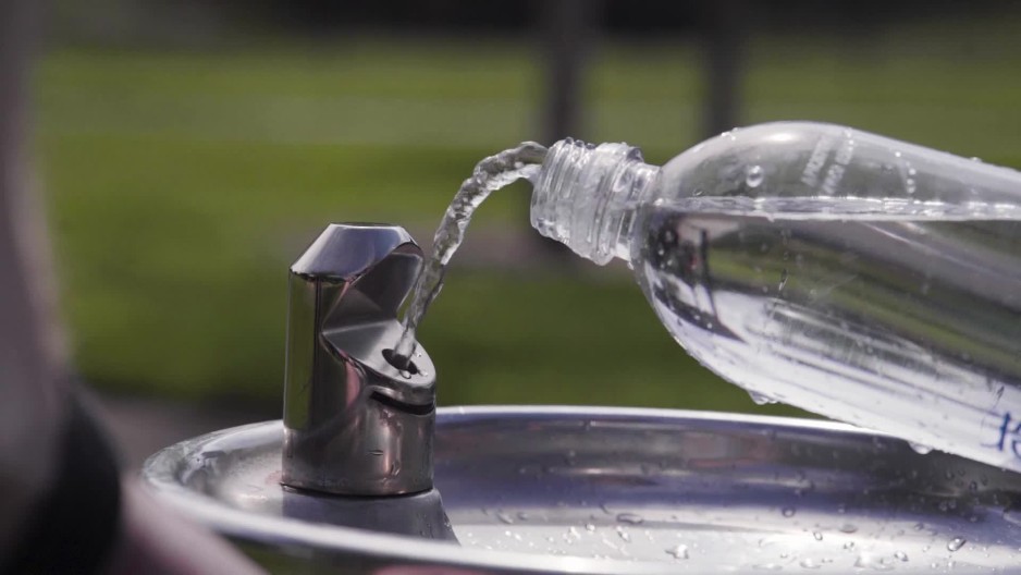 person refilling plastic water bottle at drinking fountain for reuse at