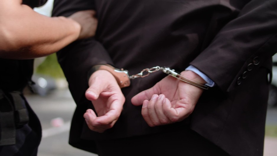 Man escorted by police with hands handcuffed behind his back | ClipStock