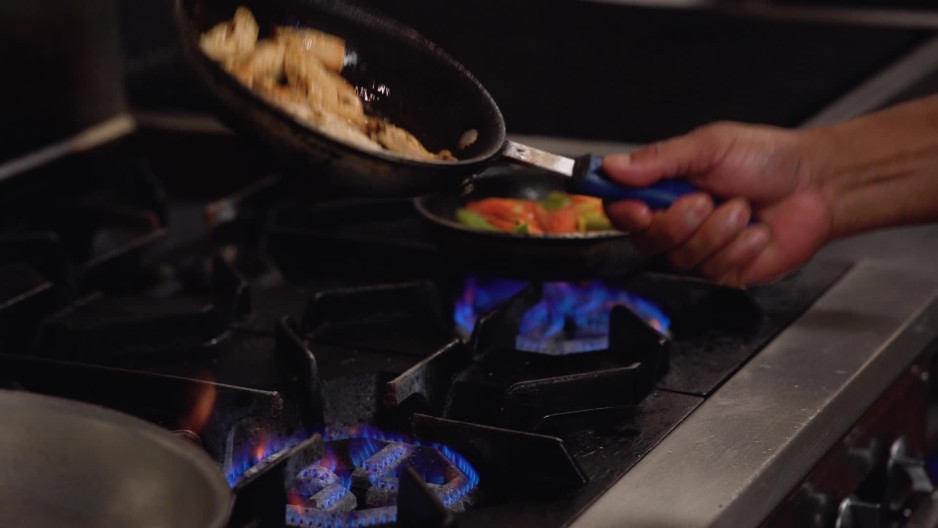 Chef flipping pan of sauteing cooking chicken on gas stove in