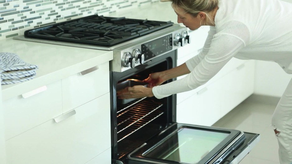 Woman putting baking pan with mixture into oven in modern kitchen