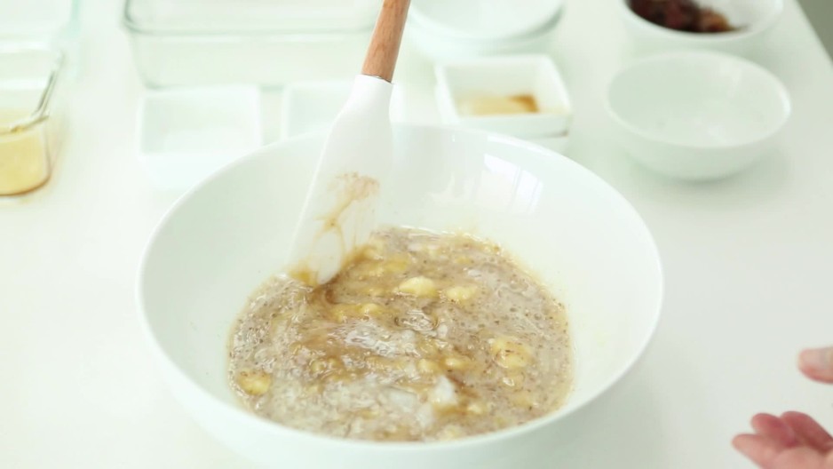 Woman using spatula to stir banana bread mixture in bowl while baking