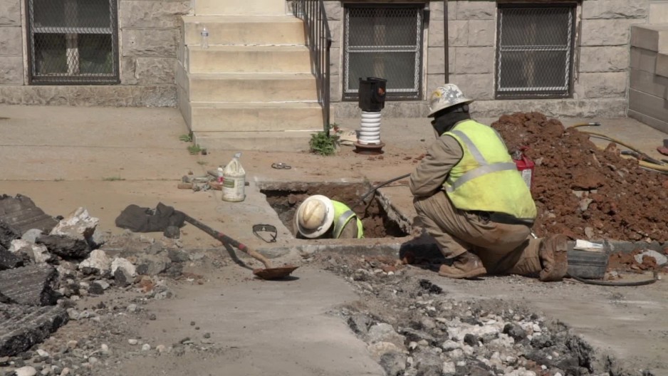 Static shot of construction worker digging under sidewalk near houses