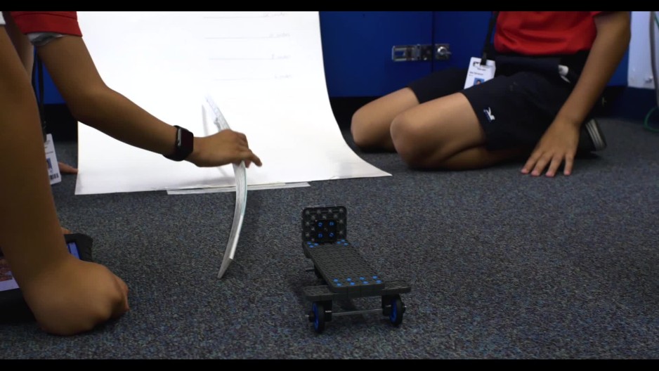 Close up of students measuring distance travelled by toy car in