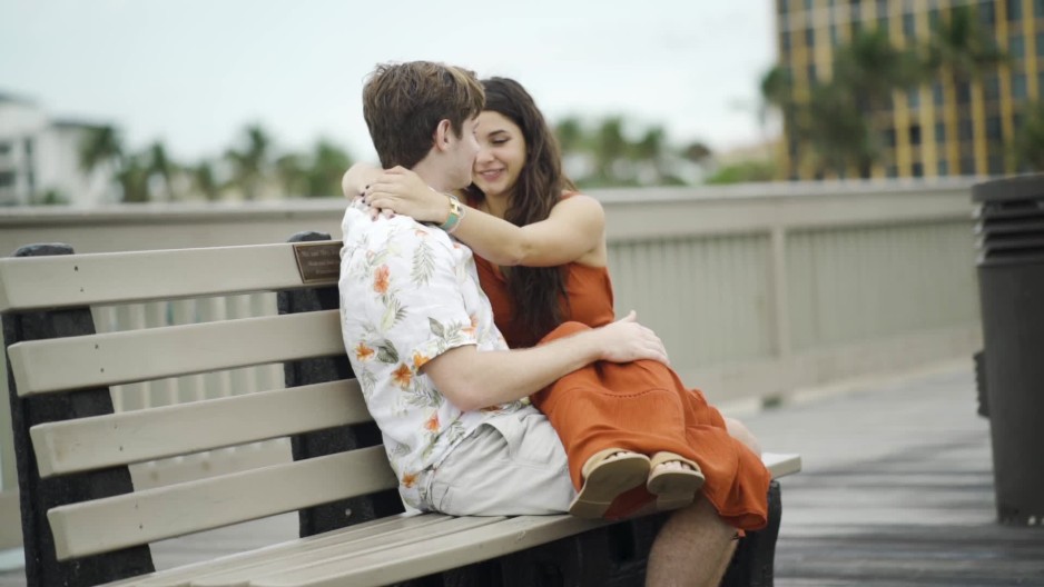 Young couple hugging each other while sitting on bench on pier slow
