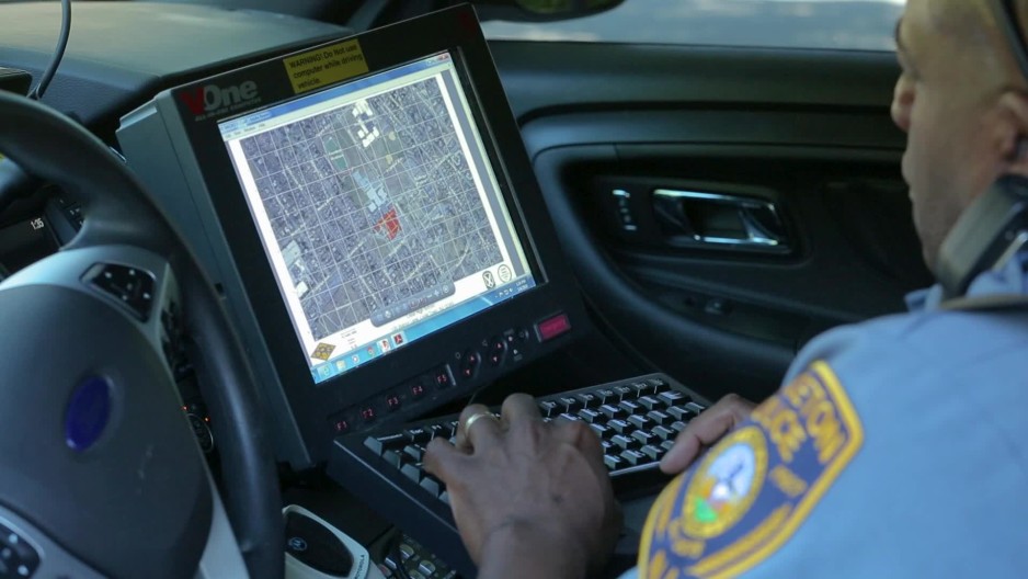 close up of a police officer using a computer mounted in his squad car