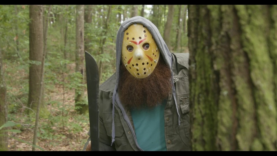 Medium shot of man in killer outfit with hockey mask standing in woods