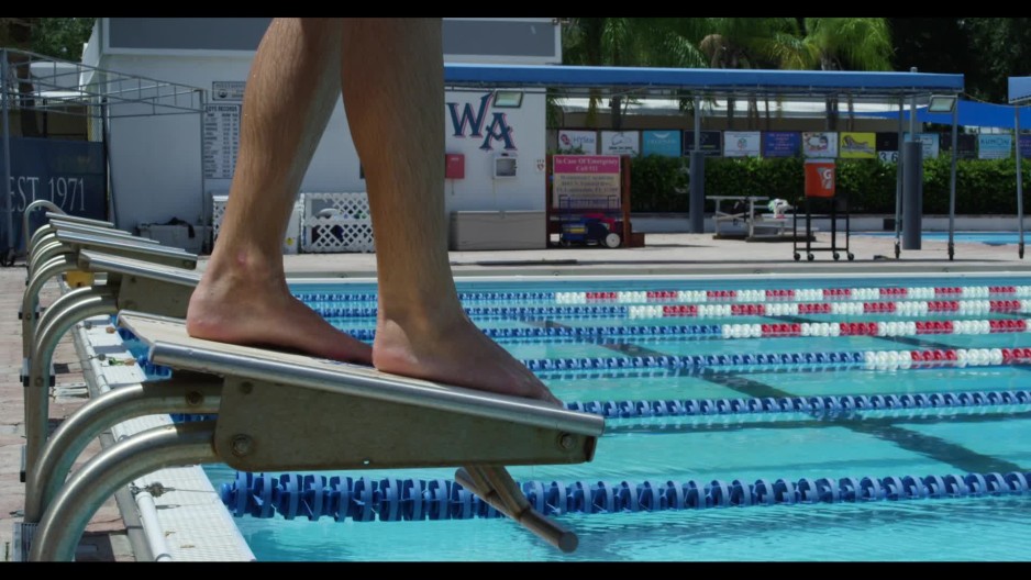 Male athlete swimmer diving off starting block into lap pool and
