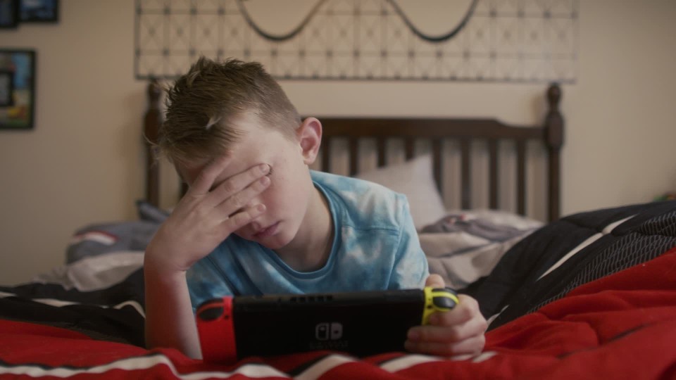 Bored little boy losing interest playing video games lying in bedroom