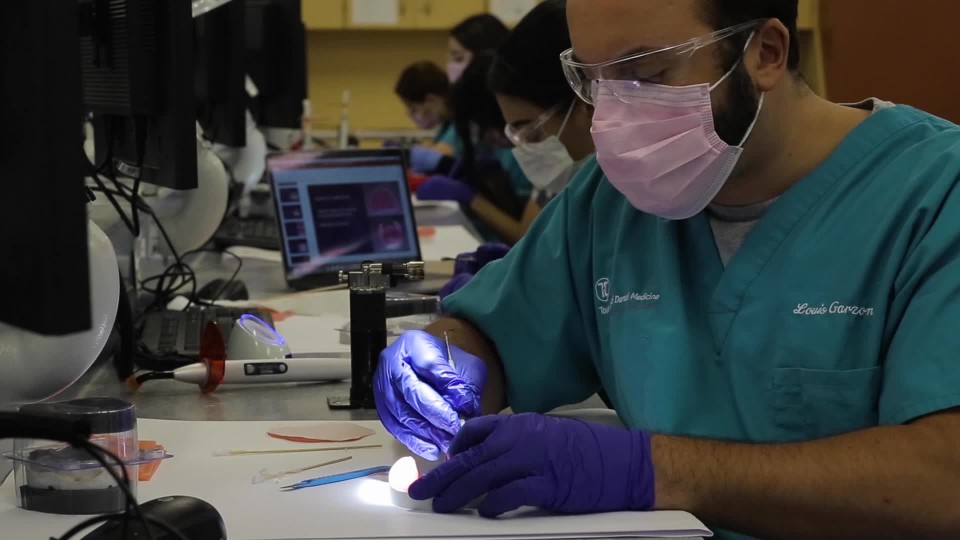 Female and male workers sculpting dental prosthetics at workbench under lights from behind