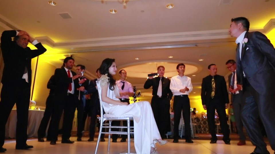 Asian groom removing garter belt from leg of bride | ClipStock