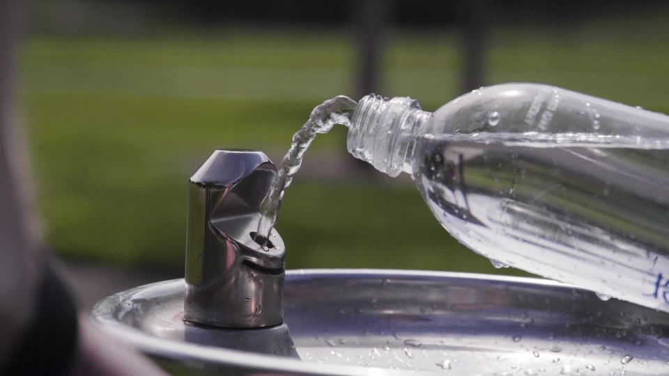 person refilling plastic water bottle at drinking fountain for reuse at