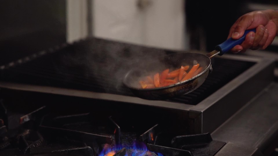 Chef flipping pan of sauteing cooking chicken on gas stove in