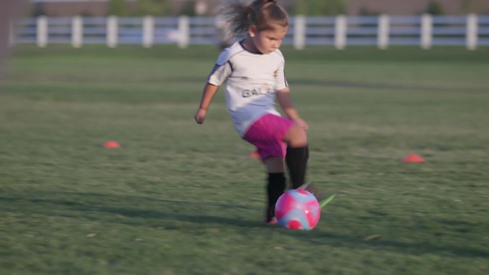 Little girl dribbling soccer ball across field during soccer practice