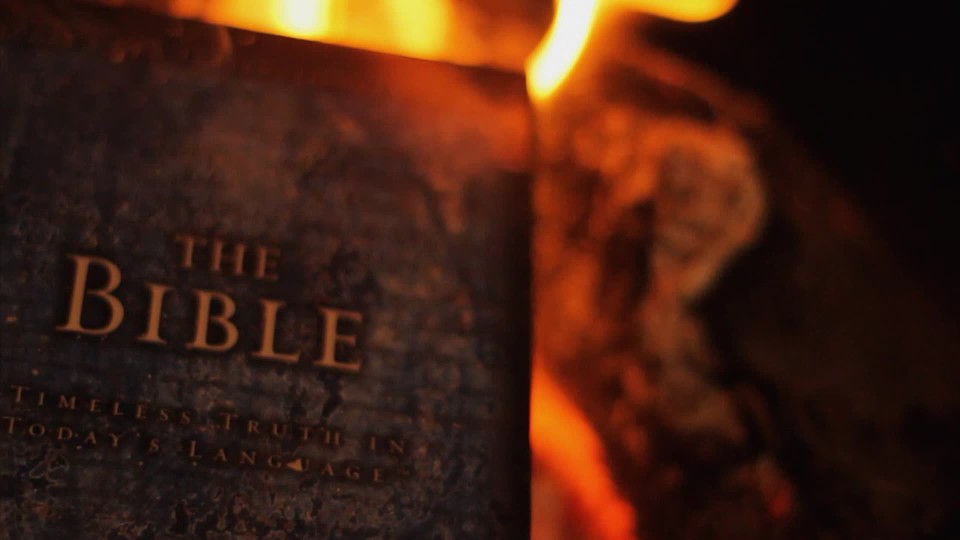 Extreme close up of the Bible with flames in the background | ClipStock