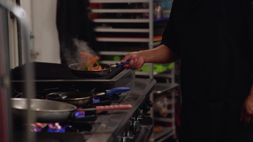 Chef flipping pan of sauteing cooking chicken on gas stove in