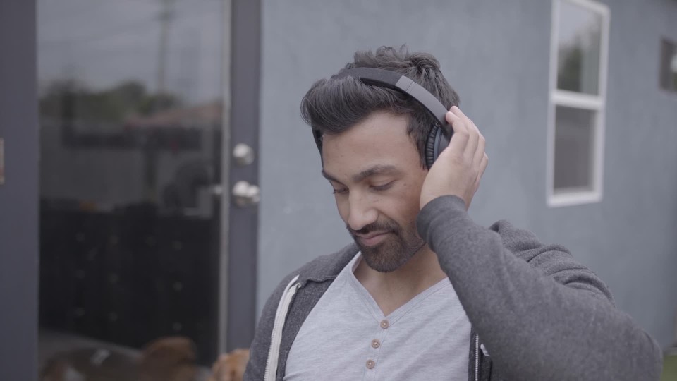 Handsome Asian man leaning on counter wearing headphones listening to