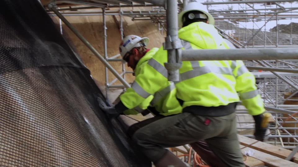 Construction workers on scaffold wearing safety gear drilling into and